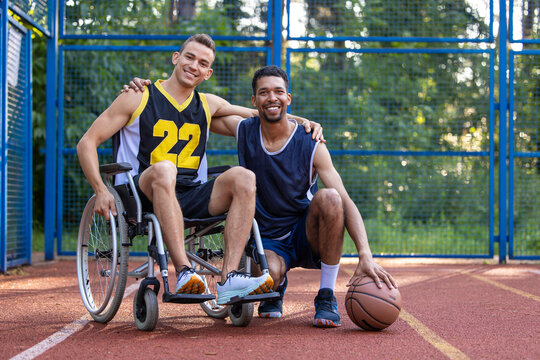 Man playing basketball with disabled friend in wheelchair at outdoor court.