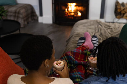 African american couple in socks relaxing at home drinking hot chocolate in front of open fire