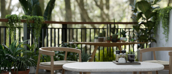 Coffee table and armchairs on a green balcony relaxation space with various tropical plants.