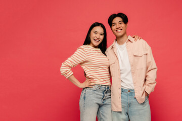 Asian man and woman smiling while standing isolated over red background
