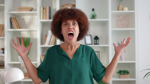 Portrait of multiethnic woman in elegant clothes screaming loudly with anger on face against bookcase background. Overwhelmed adult lady reducing escalating rage by yelling with following relief.