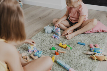 Children playing with colorful wooden toy train. Kids sitting on carpet at home bedroom, kindergarten, daycare playroom, playground, play center. Funny educational eco-friendly game for child - obrazy, fototapety, plakaty