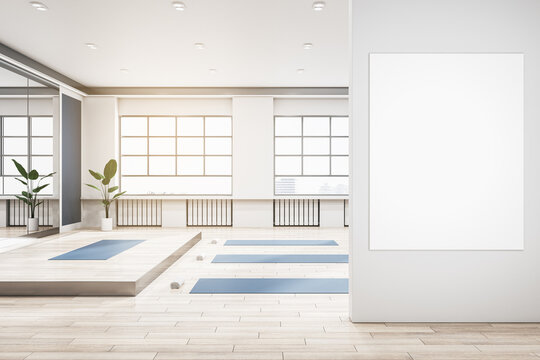 Modern group class in gym interior with blank white mock up banner on wall, blue yoga mats, wooden flooring, mirror with reflections, window with city view and daylight. 3D Rendering.