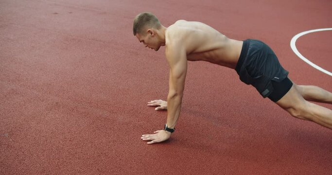 Muscular Man Has Cross Fit Training And Doing Plank Exercise With Shoulder Tap Outdoors At Sports Ground. Young Athletic Male Has Intense Workout Outside