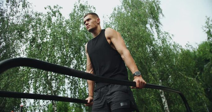 Athletic man has workout, hanging and pull up on parallel bars outdoors. Young sporty male with muscular body exercising on sport ground at park.