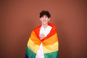 Young attractive man posing with a rainbow flag. Brown background.