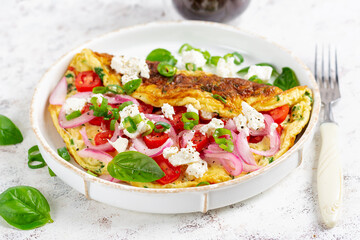 Omelette with tomatoes, feta cheese and red onion on white plate.  Frittata - italian omelet.