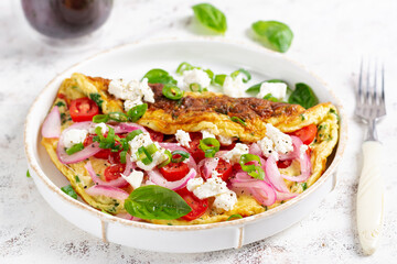 Omelette with tomatoes, feta cheese and red onion on white plate.  Frittata - italian omelet.