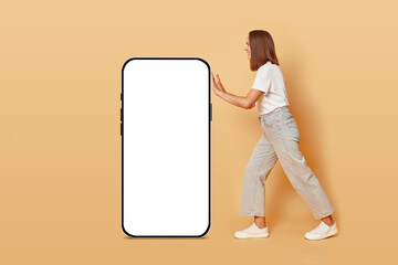 App service. Social media influencer. Online shopping experience. Happy cheerful brown haired adult woman pulling big phone with white empty display isolated over beige background