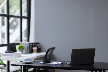 Laptop Computer, notebook, and eyeglasses sitting on a desk in a large open plan office space after working hours

