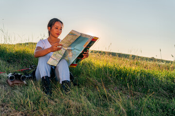 young beautiful woman is sitting in the grass, resting and reading a map