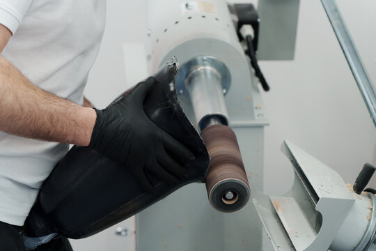 Closeup of unrecognizable master in gloves working on prosthetic limb while shaping and forming it on sanding machine in modern workshop