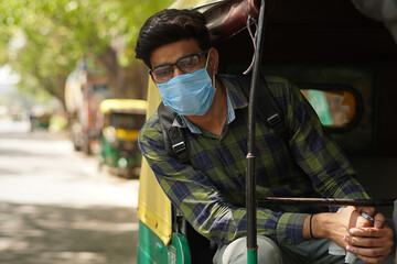 Young Indian middle class young man travelling in auto rickshaw using face mask - obrazy, fototapety, plakaty
