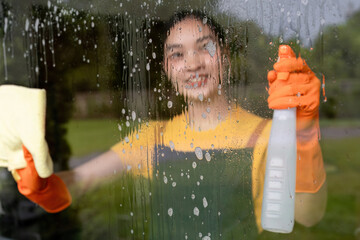 Cleaning the house of a housewife who is wiping the glass using a cleaning spray and a cloth