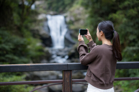 Woman use of mobile phone to take photo with waterfall in forest