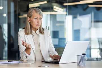 Dissatisfied and disappointed senior gray haired business woman at workplace, female boss received online notification on laptop about poor and unsatisfactory achievement results.