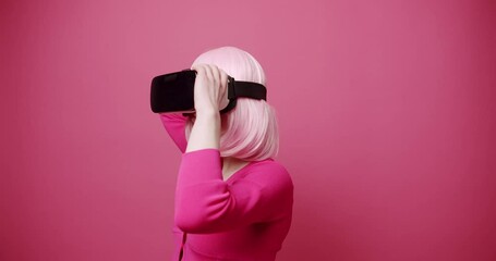 Woman uses a virtual reality glasses, seek and touch in virtual life on isolated pink background. Concept of future, innovation, technology, gaming, lifestyle, entertainment. Pink Colors. Modern Woman