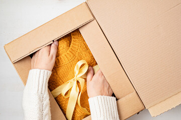 Unpaking delivery box with warm orange sweater inside. Online shopping, gifts for fall and winter seasonal holidays, christmas