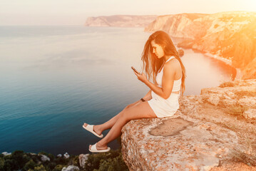 Happy woman in white shorts and T-shirt, with long hair, talking on the phone while enjoying the scenic view of the sea in the background.