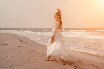 Fototapeta na wymiar woman sea white dress. Model in boho style in a white long dress and silver jewelry on the beach. Her hair is braided, and there are many bracelets on her arms.