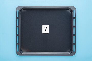 Dark black oven tray with white card of question mark on light blue table background. Pastel color. Closeup. Top down view. Cooking concept.