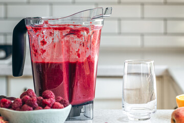 Blender with red berry smoothie and an empty glass on the kitchen table.