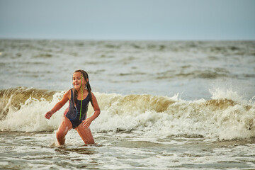 Little girl playing with waves in the sea. Kid playfully splashing in waves. Child jumping in sea. Vacations on the beach. Water splashes
