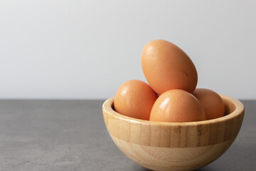 Four Fresh Eggs Stacked in Bamboo Bowl on Gray Table (With Copy Space)