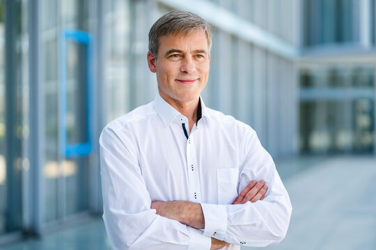Casual businessman standing in front of office building with arms crossed