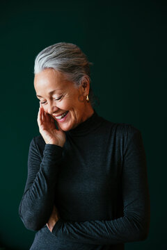 Happy Mature Woman Touching Face In Front Of Wall