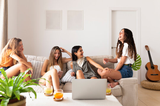 Friends sitting on sofa with laptop and laughing at home - Powered by Adobe