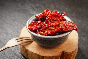 Close-up of a bowl of sun-dried tomatoes in olive oil on a gray stone background. Studio shot.