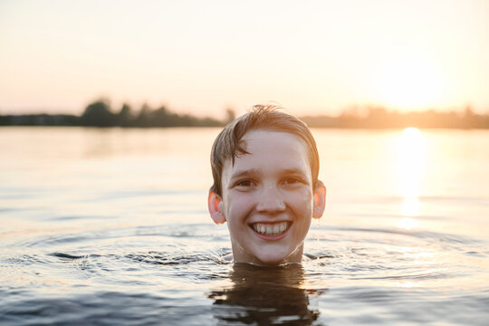 Smiling boy swimming in lake water at sunset
