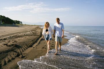 Couple walking barefoot at beach on sunny day