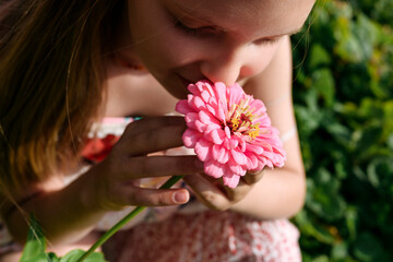 Girl holding and smelling pink flower in garden