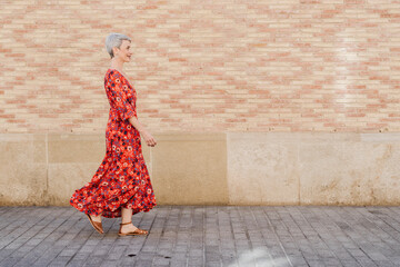 Smiling woman wearing red dress walking in front of wall