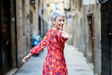 Smiling woman wearing red dress beckoning in alley