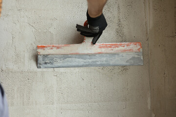 Rear view of handyman worker plastering concrete wall with putty using a big putty knife....