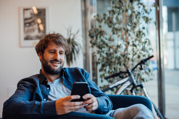 Smiling businessman using smart phone in office