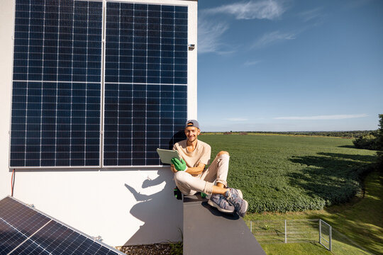 Man sitting on a rooftop and using digital tablet monitoring production from the solar power station installed on his property. Concept of modern technologies and sustainable lifestyle