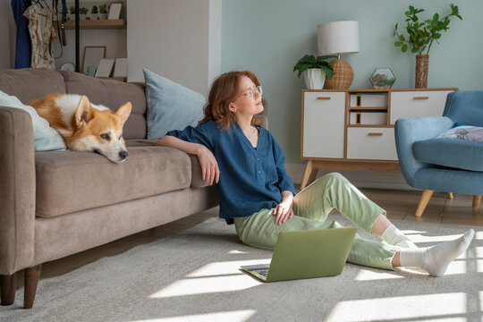 Thoughtful freelancer with Welsh Corgi dog on sofa at home