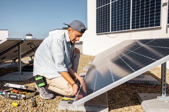 Man installing solar panels on the roof of his house, screwing cell on flat rooftop for self consumption. Renewable energy and sustainability concept