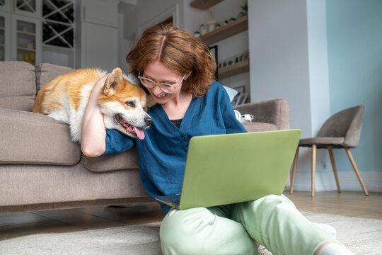 Smiling freelancer with laptop embracing pet dog in living room