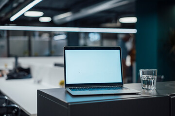 Laptop and glass of water on desk in office