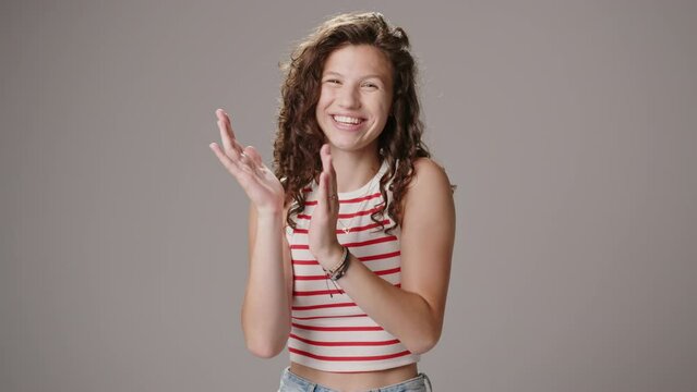 Beautiful young female model with long curly brown hair looks and smiles at the camera in the studio. A headshot with a sexy model claps the hands. Slow motion.