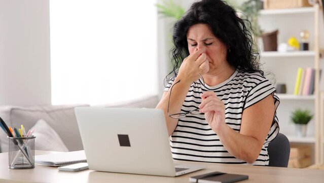 Middle aged woman working at home on laptop while suffering eye fatigue. Overworking and presbyopia concept.