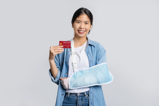 Young beautiful asian office worker in cast due to broken arm in accident while holding credit card isolated on white background. Accident insurance or medical expenses concept.