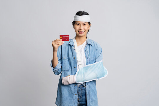 Happy smile asian woman with broken head and wearing soft cast due to broken arm showing credit card isolated on white background. Accident insurance or medical expenses concept.