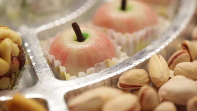 Close-up of different types of Indian sweets, dry fruits, and namkeen revolving on a silver paper plate.