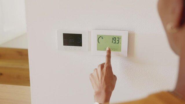 Ethnic woman adjusting smart thermostat control on wall